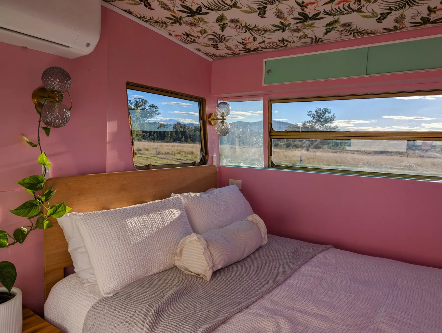 The double bed in the van, pink walls and floral ceiling, windows onto the paddock