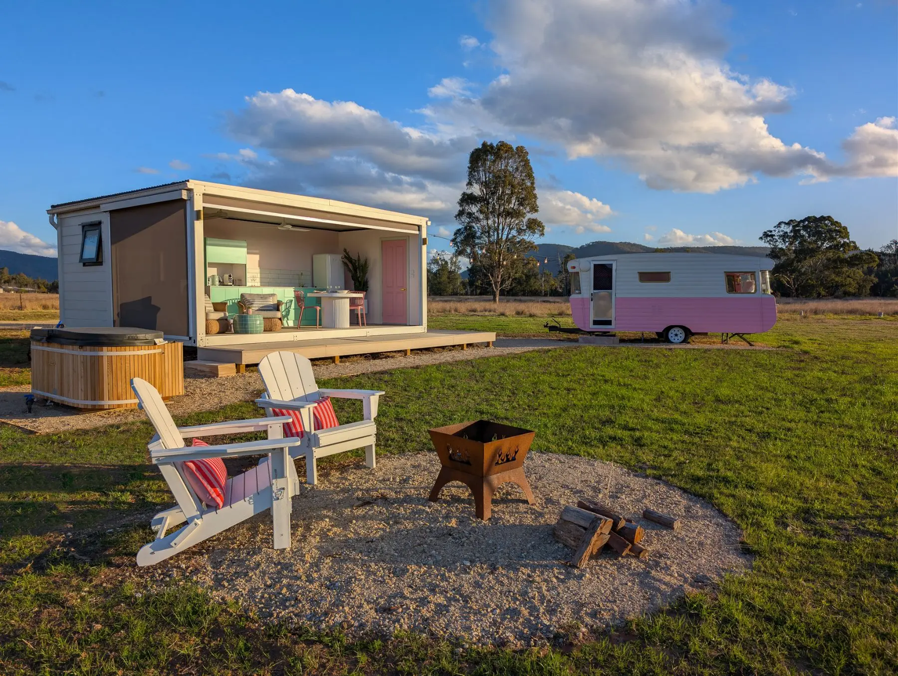 The pavilion open to the deck with the pink caravan beyond, firepit and outdoor bath in the foreground