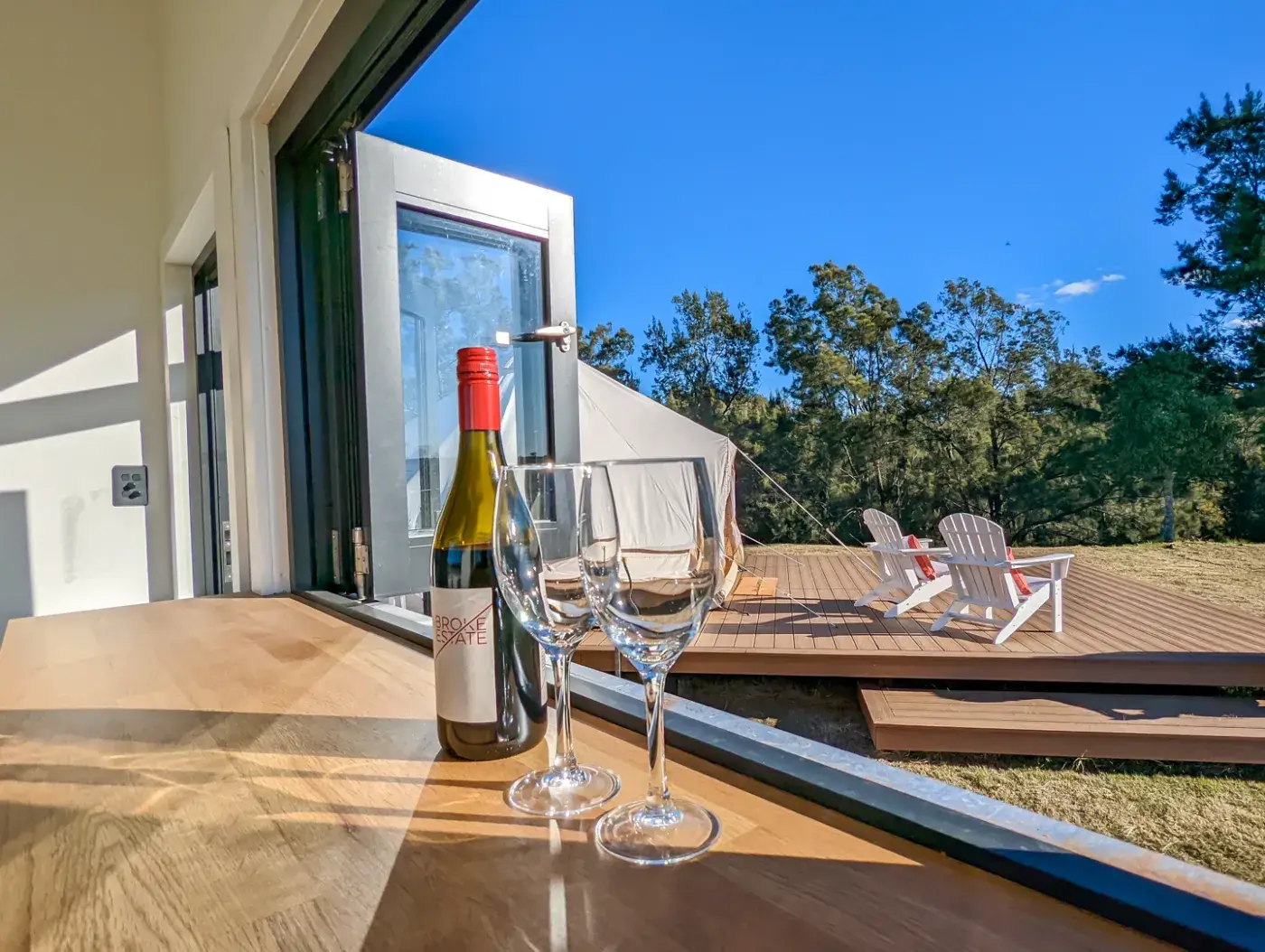A bottle and two glasses on the pod bench, the tent and deck chairs through the open door