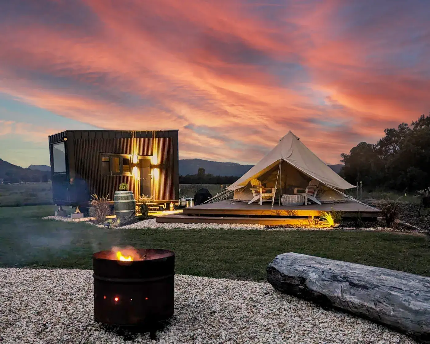 The Bell Tent and the amenities pod lit up at sunset, firepit burning in the foreground