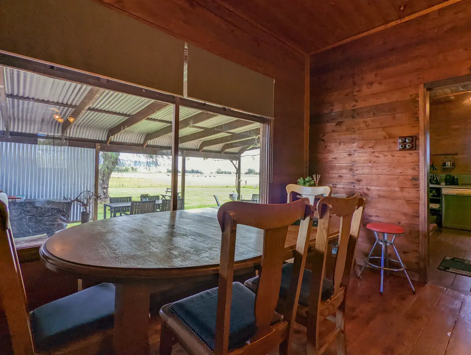 The Cottage dining table set in timber-lined walls, with the undercover verandah and cattle paddocks through the window