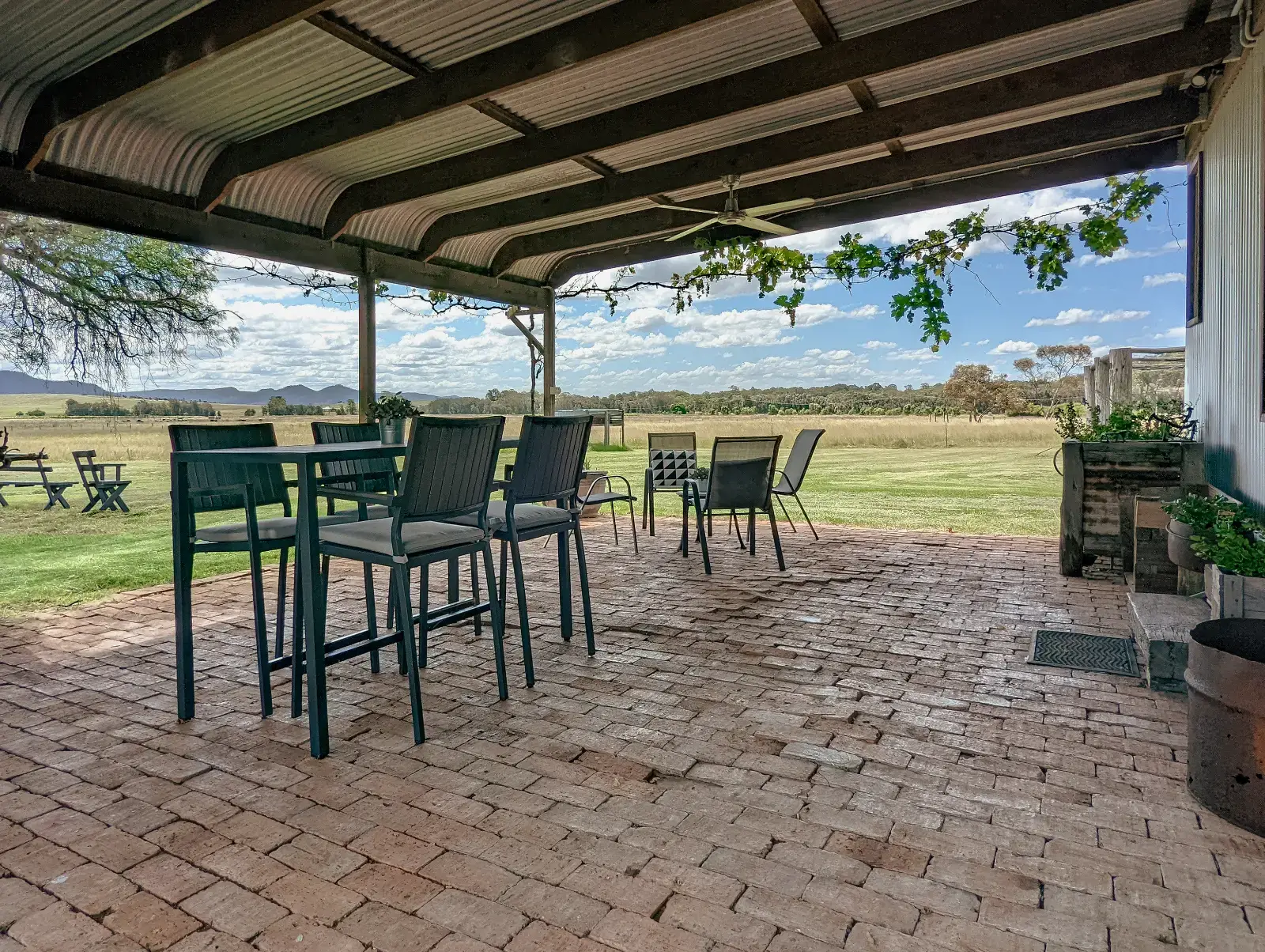 A long table on the Cottage verandah under the iron roof, paddocks and the ranges beyond