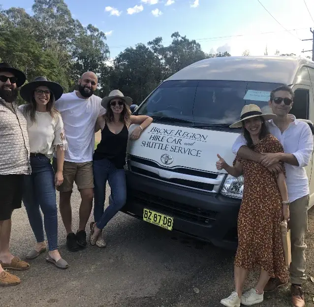 A group of guests smiling beside the Broke Region Hire Car and Shuttle Service van
