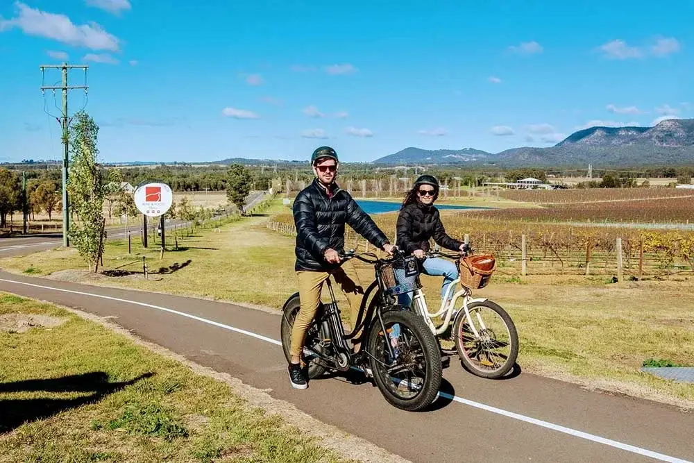 Two riders on e-bikes on the cycle path beside the vineyards on Hermitage Road, Pokolbin