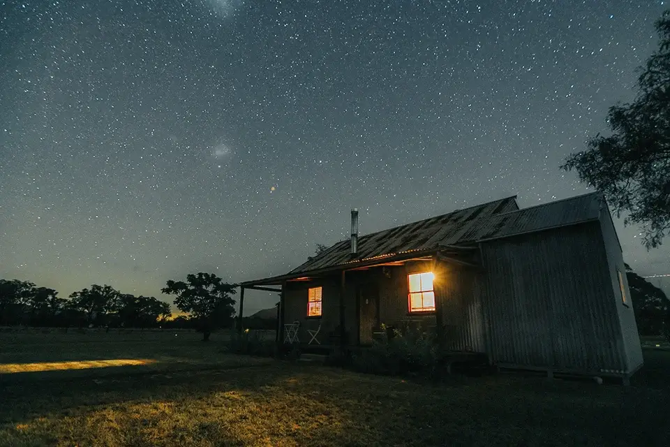 The Cottage lit from within under a sky full of stars at Broke Estate